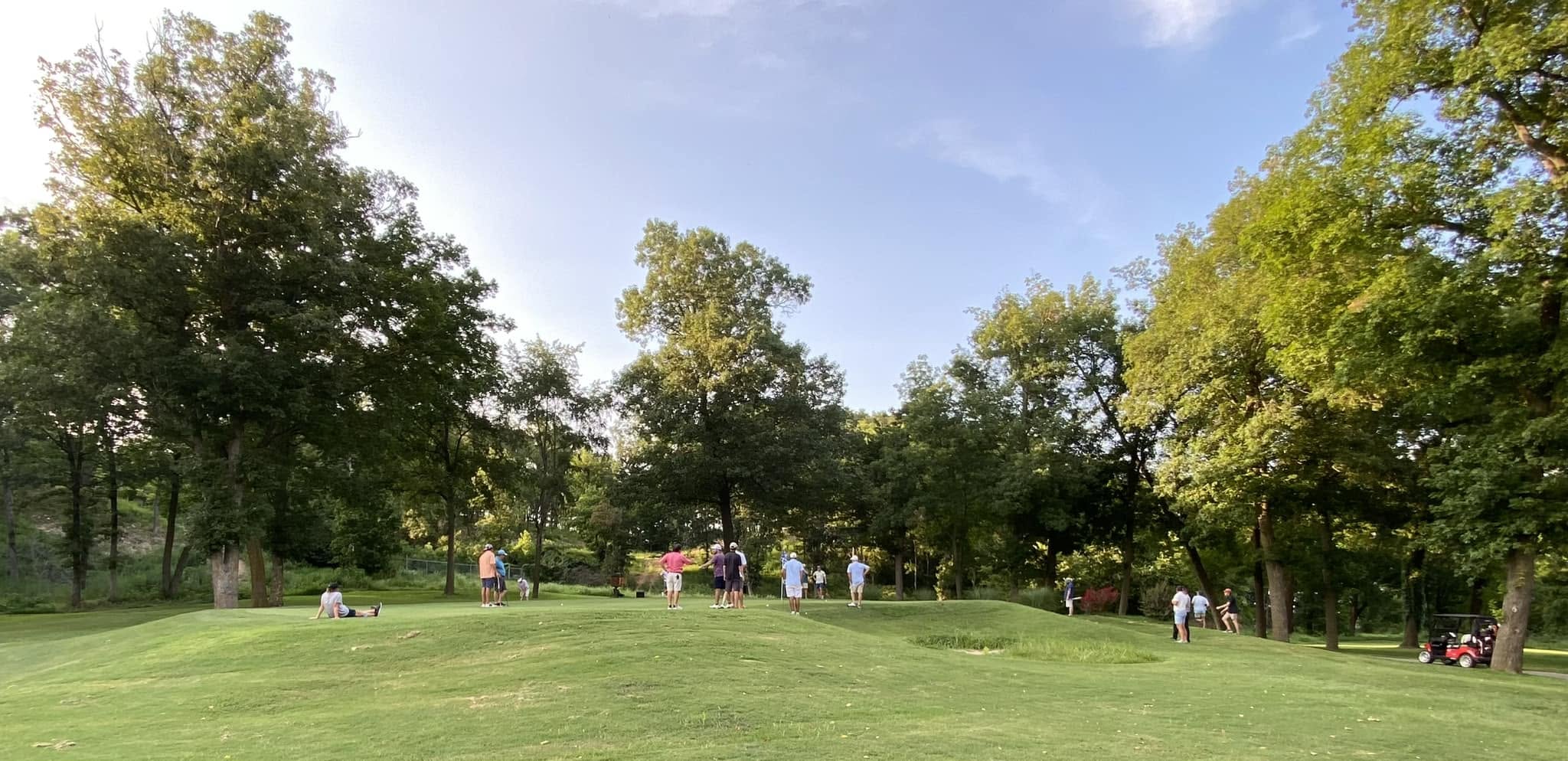 A tree-lined fairway with golfers and a cart